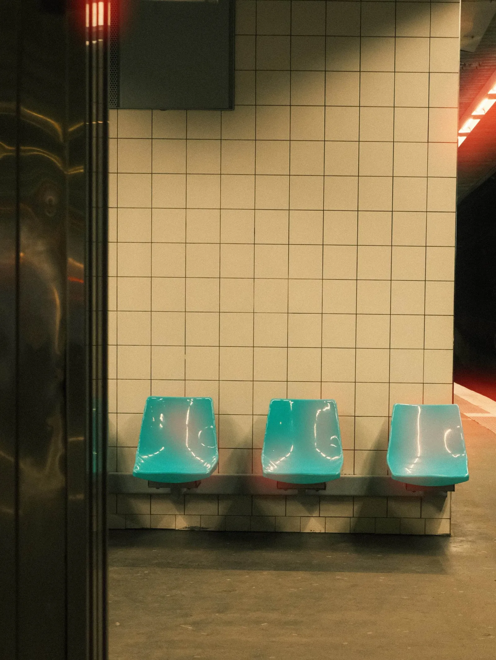 Metro platform with turquoise seats and a warm red halation glow from the tunnel lights