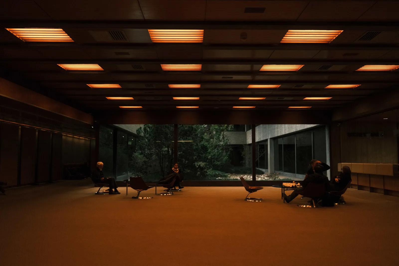 Dark modernist lounge at the Gulbenkian in Lisbon, orange ceiling light panels above low chairs and a garden behind the glass