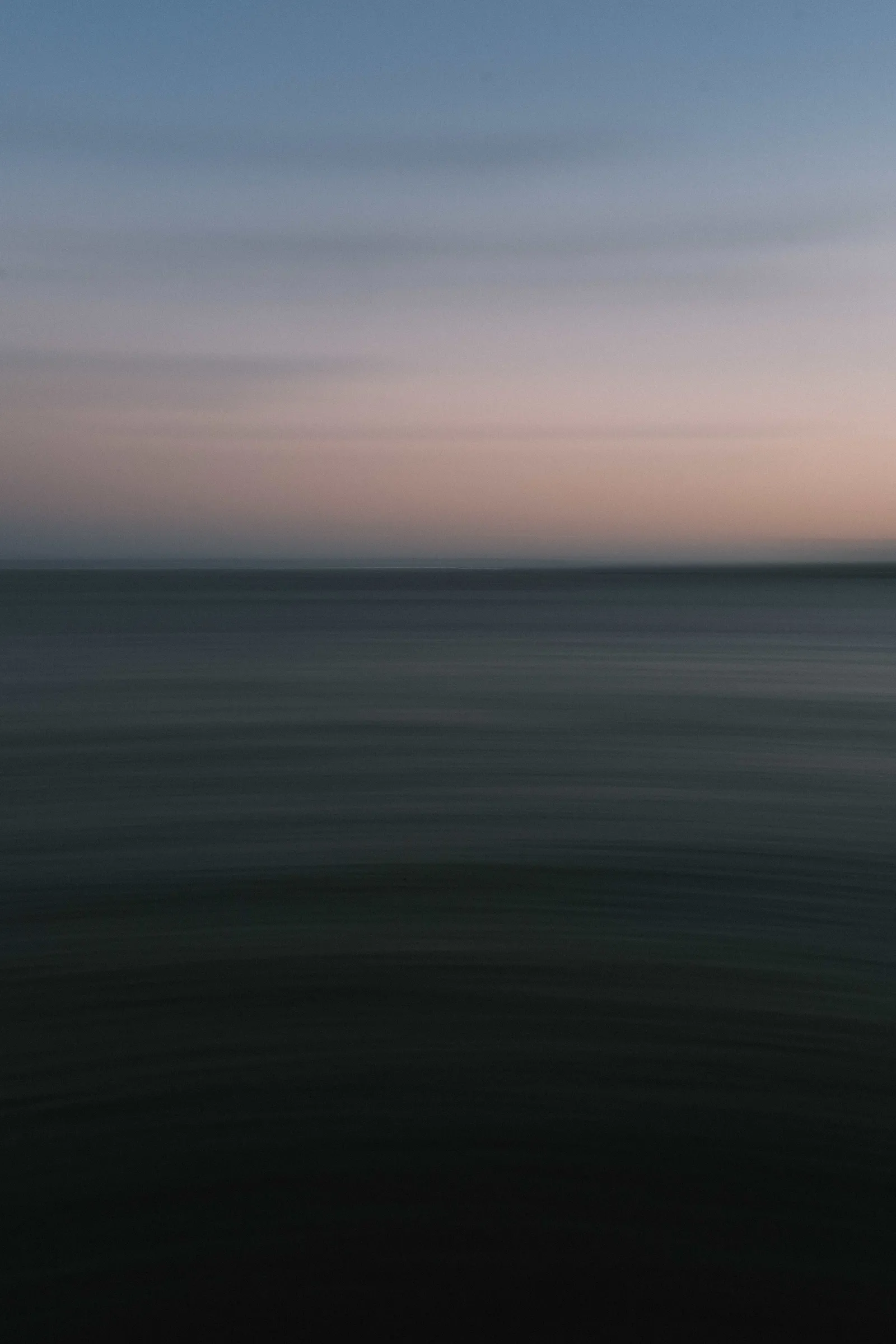 Long exposure of the sea at dusk, pink and blue bands blurred into flat horizontal colour