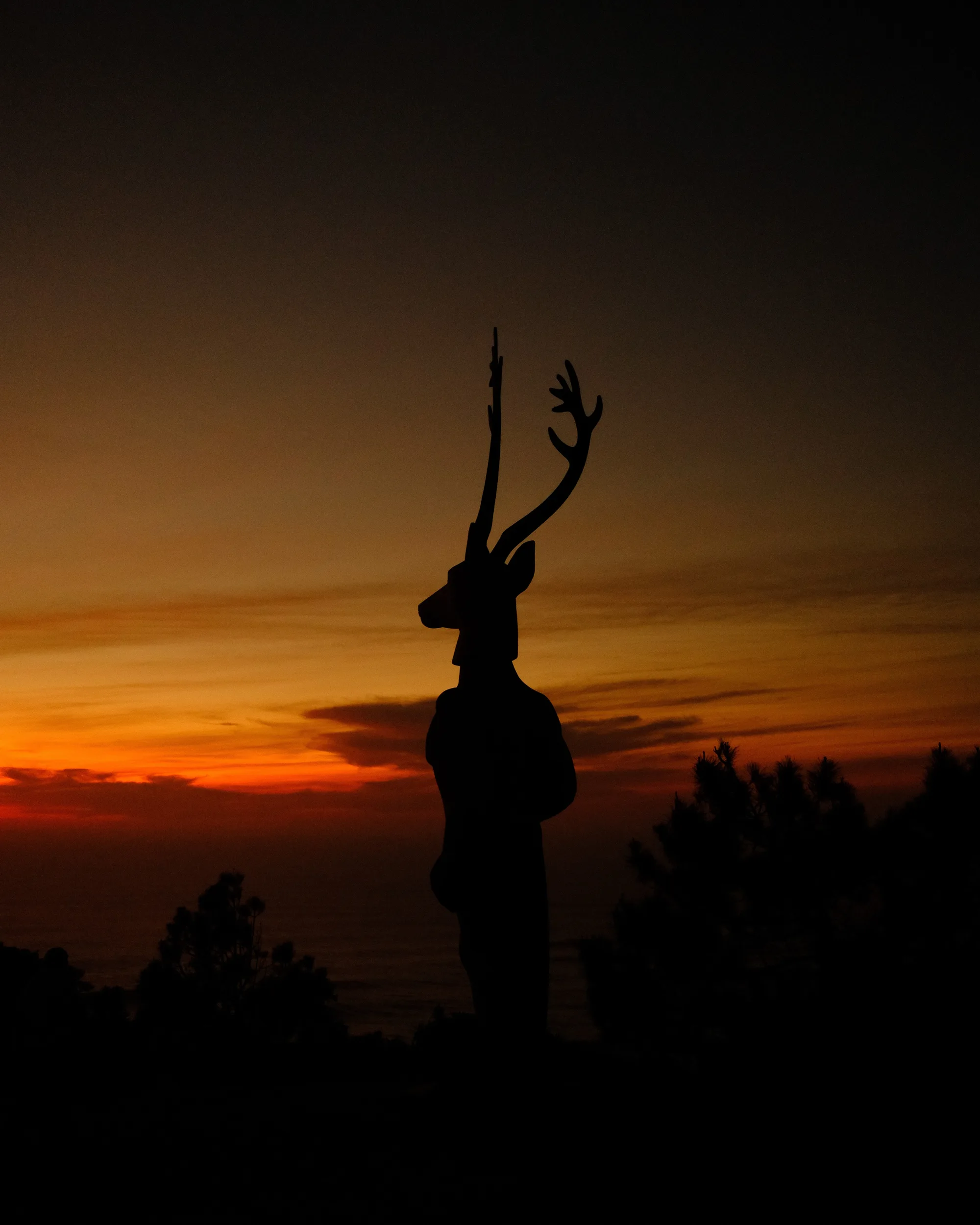 Deer-headed statue silhouetted against a red and orange sunset - Velvia SOOC recipe by xere.my