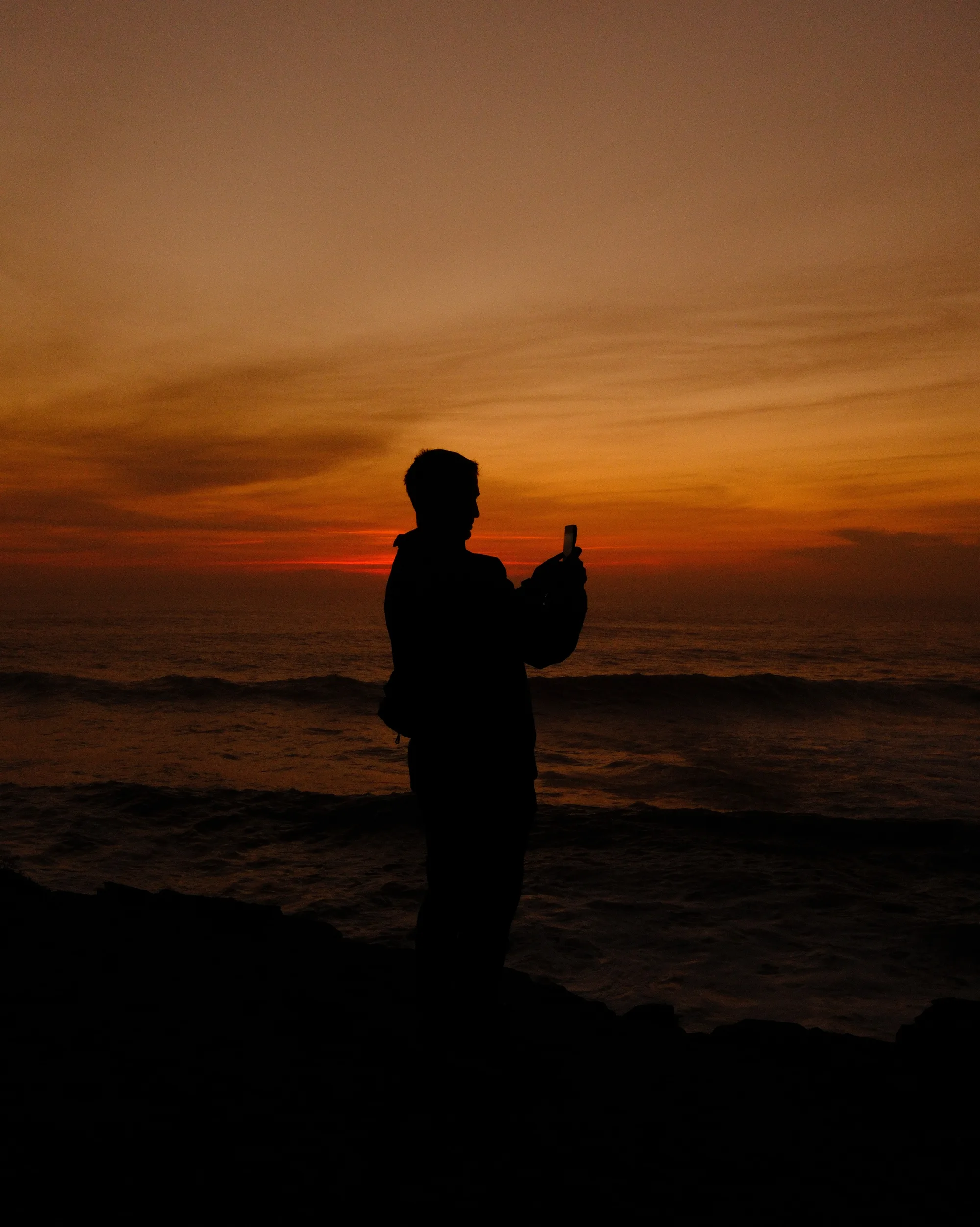 Silhouette of a person filming the sea after sunset with an orange sky - Fujifilm Burning recipe